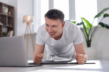 Evde bilgisayarla yoga dersi alan bir adam.