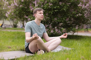 Genç adam parkta yoga yapıyor.