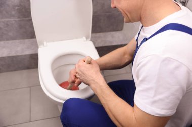 Tesisatçı tuvalet tıkanıklığını açıyor, içeride pompa var, yakın plan.