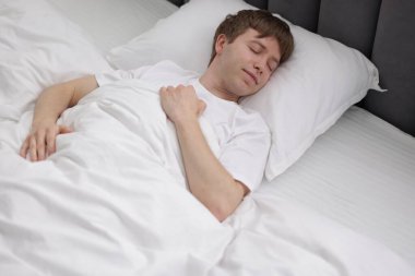 Genç adam yatağında uyuyor.