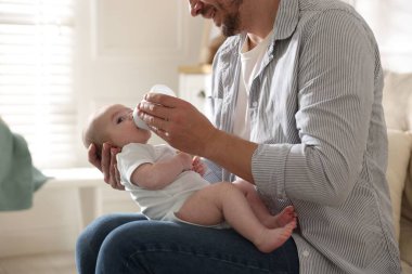 Babası evdeki kanepede bebeğini biberonla besliyor.