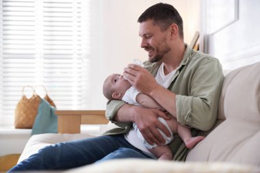 Babam evdeki kanepede bebeğini biberonla besliyor. Metin için boşluk