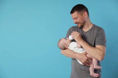 Baba bebeğini açık mavi arka planda bir şişeyle besliyor. Metin için boşluk