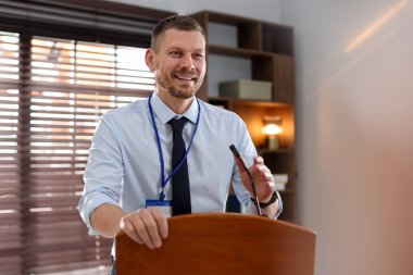 İçerideki kürsüde mikrofonla halka açık konuşma yapan adam.