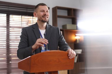 İçerideki kürsüde mikrofonla halka açık konuşma yapan adam.