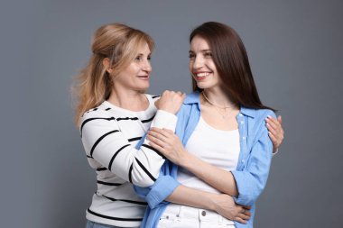 Anne ve kızı gri arka planda sarılıyorlar.