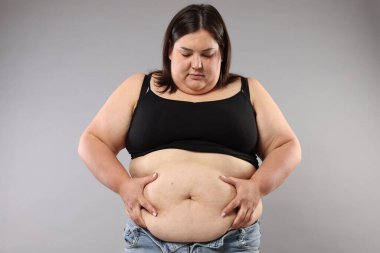 Gri arka planda aşırı göbek yağlı bir kadın. Aşırı kilolu
