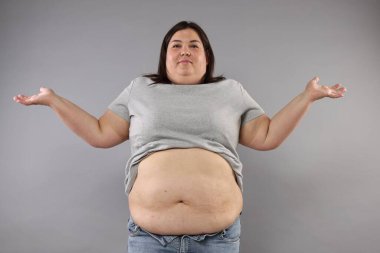 Gri arka planda aşırı göbek yağlı bir kadın.