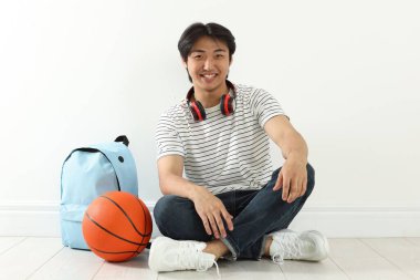 Kapalı alanda basketbol topu ve sırt çantası olan mutlu bir öğrenci.