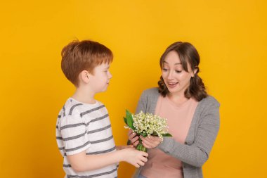 Çocuk sarı arka planda annesine güzel bir çiçek buketi veriyor.
