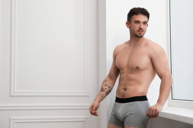 Beyaz duvarın yanındaki açık gri iç çamaşırlı genç adam. Metin için boşluk