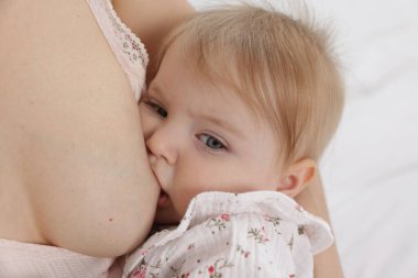 Anne küçük bebeğini yatakta emziriyor, yakın plan.