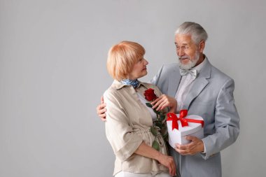 Hediye kutusu olan ve açık gri arkaplanda gül gülü olan sevimli yaşlı çift, mesaj için yer var.