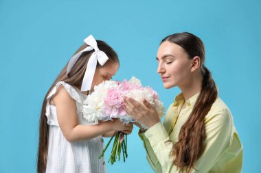 Sevimli küçük kız annesine açık mavi arka planda şakayık demeti veriyor.