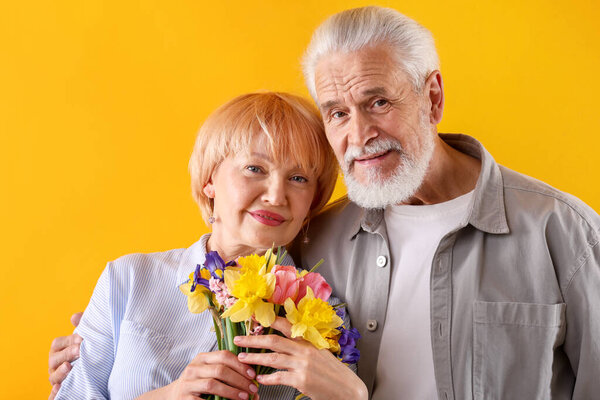 Lovely senior couple with bouquet of flowers on yellow background
