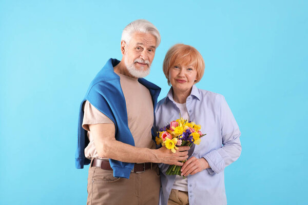 Lovely senior couple with bouquet of flowers on light blue background