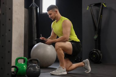 Spor salonunda klasörlü ve spor aletli kişisel antrenör.