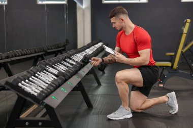 Spor salonunda klasörlü ve dambılı kişisel antrenör.