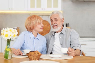 Mutfaktaki ahşap masada birlikte kahvaltı eden sevimli yaşlı çift.
