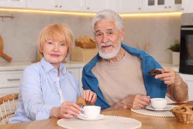 Mutfaktaki ahşap masada birlikte kahvaltı eden sevimli yaşlı çift.