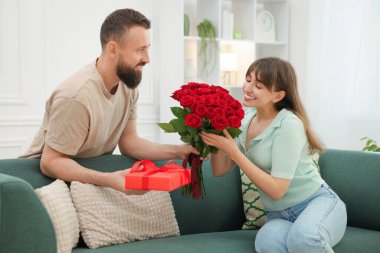 Evdeki sevgilisine kırmızı gül buketi ve hediye kutusu sunan bir adam.