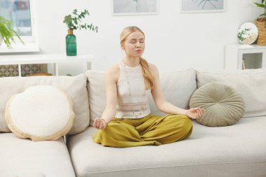 Feng shui. Evdeki kanepede meditasyon yapan genç bir kadın.