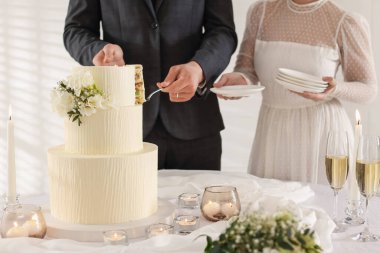 Damat düğün pastasından bir parça alırken gelin tabakları içeride tutuyor, yakın plan.