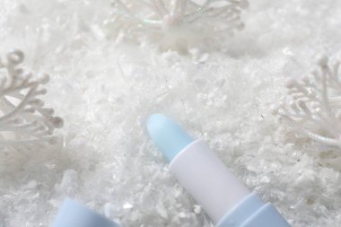 Nemlendirici dudak kremi ve yapay kar üzerine Noel süsü, yakın plan. Kış bakımı