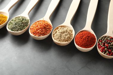 Gri masadaki kaşıklardaki farklı baharatlar, yakın plan.