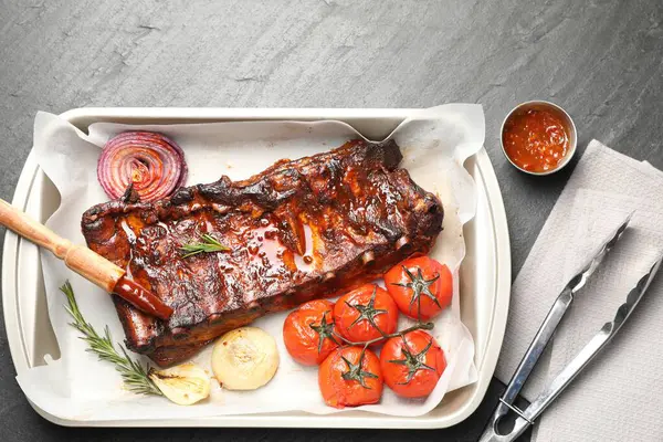 Lezzetli kaburgalar, fırında soğan, kurutulmuş güneş domatesleri ve gri desenli masada sos.
