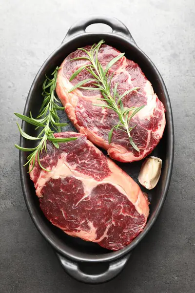 Çiğ et parçaları ve baharatlar gri desenli masa üzerinde fırın kabında, üst görünüm