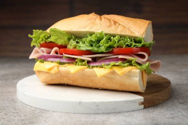 Gri desenli masada jambonlu, peynirli ve sebzeli baget sandviç, bulanık kahverengi arka plan, yakın plan.