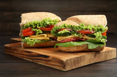 Lezzetli baget sandviç parçaları füme sosis, peynir ve sebzeler ahşap masada, yakın plan.