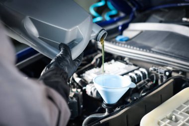 İşçi motor yağını teneke kutudan araba motoruna boşaltıyor.
