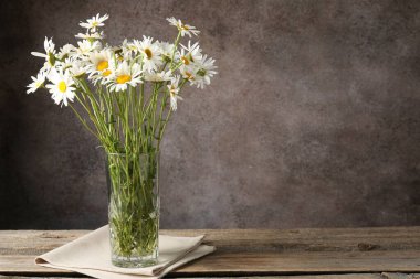 Tahta masadaki vazoda bir sürü güzel papatya çiçeği kahverengi desenli arka planda, yakın plan. Metin için boşluk