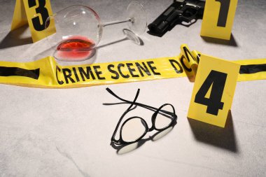 Adli tıp uzmanlığı. Açık gri arka planda delil, işaret ve polis bandı olan suç mahalli, yakın plan