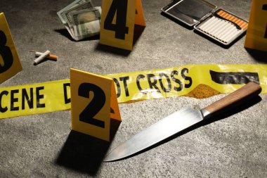 Adli tıp uzmanlığı. Gri arka planda delil, işaret ve polis bandı olan olay yeri, yakın plan.