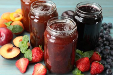 Kavanozlardaki farklı reçeller ve mavi ahşap masa üzerindeki malzemeler, yakın plan.