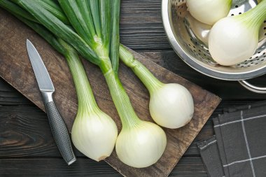 Taze taze soğanlar, kesme tahtası ve bıçakla siyah ahşap masa, düz yatıyordu.