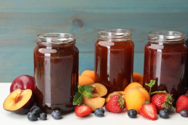 Kavanozlardaki farklı reçeller ve malzemeler beyaz masada, yakın plan.