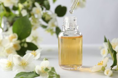 Şişeye yağ damlatıyor ve beyaz masada güzel yasemin çiçekleri, yakın plan.