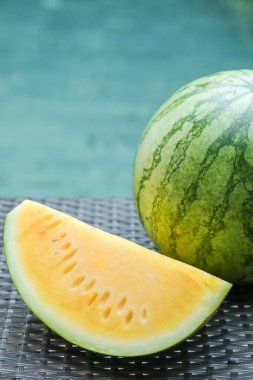 Açık havuzun yanındaki hasır masada sarı karpuzlar var. Yakın plan.