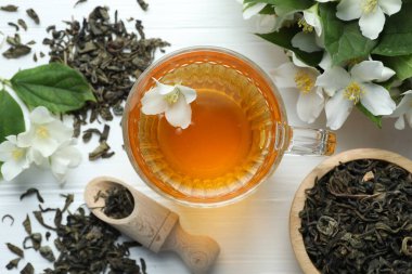 Cam bardakta Aromatik yasemin çayı, beyaz ahşap masada çiçekler ve yapraklar, düz uzanmış