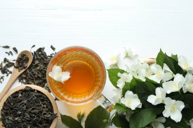 Cam bardakta Aromatik yasemin çayı, beyaz ahşap masada çiçekler ve yapraklar, düz uzanmış