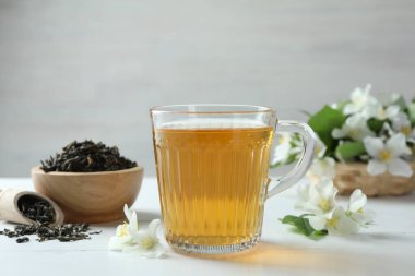 Cam bardakta yasemin çayı, beyaz ahşap masada çiçekler ve kuru yapraklar, yakın plan.