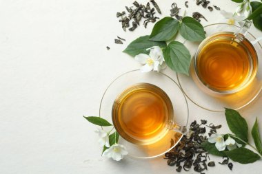 Camdan fincanlar içinde yasemin çayı, beyaz masa üzerinde çiçekler ve yapraklar. Metin için boşluk