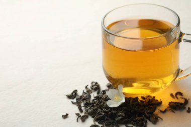 Cam bardakta Aromatik yasemin çayı, beyaz masada çiçek ve kuru yapraklar, yakın çekim. Metin için boşluk