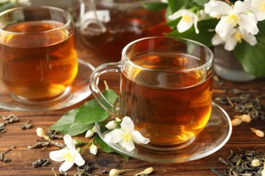 Cam fincanlarda yasemin çayı, çaydanlık, bira ve çiçekler ahşap masada, yakın plan.