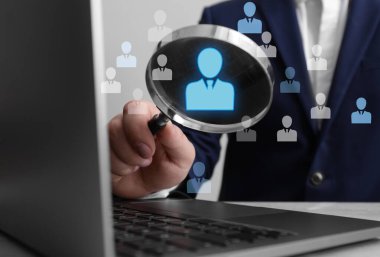 Çalışan araması. Ahşap masada dizüstü bilgisayarın yanında büyüteç tutan adam, yakın plan. Aday olarak insan simgeleri