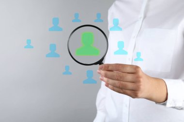 Çalışan araması. İnsan kaynakları yöneticisinin elinde gri arkaplan ve yakın plan görüntülerine karşı büyüteç var